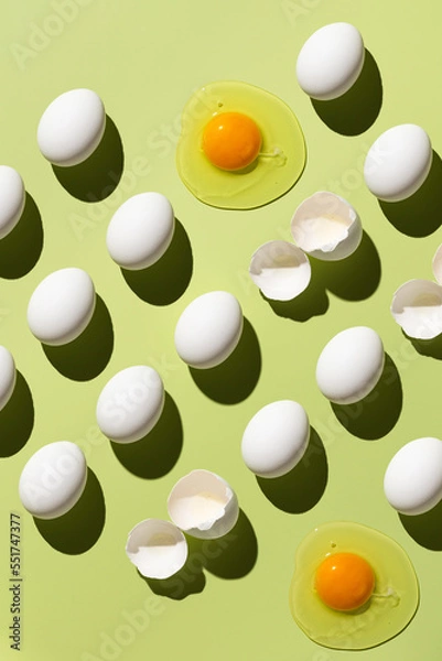 Fototapeta White eggs and egg yolk on a green background. Pattern of eggs. Broken eggs. View from above.