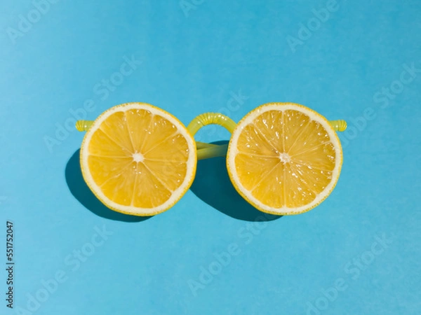 Fototapeta Yellow sunglasses made from fresh lemon slices and plastic lemonade straws on bright blue background. Summer minimal concept with sharp shadows. Funny idea