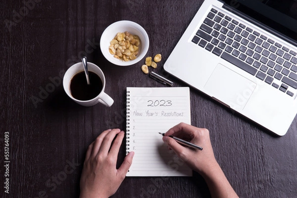Fototapeta Conceptual,Top view office desk mockup: laptop, notebook, smartphone, snack bean, and cup of coffee on rustic brown wooden desk with hand writing. New year 2023 resolution