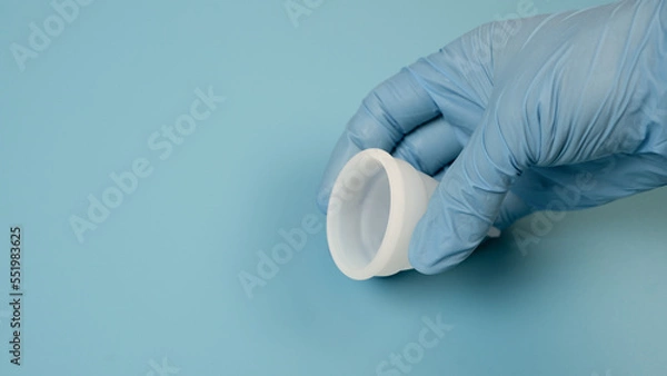 Obraz A hand in a medical, latex glove holds a hygienic, menstrual cup. Women's health concept.