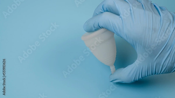 Fototapeta A hand in a medical, latex glove holds a hygienic, menstrual cup. Women's health concept.