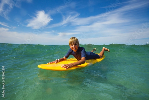 Fototapeta Happy boy lay on surf board smiling and looking at camera