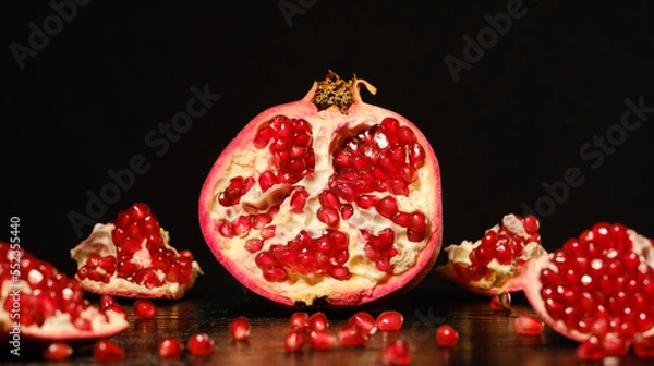 Fototapeta broken pomegranate with red ripe kernels on the table on a black background