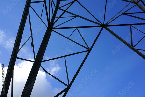 Fototapeta abstract shapes of an electric tower structure. close up of electricity pylons and blue sky backdrop. energy and power background 