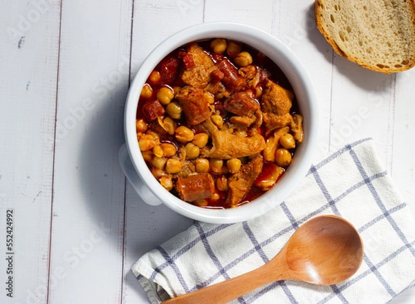 Obraz  Top view of a casserole of tripe with chickpeas on a white wooden background whith rustic spoon. Winter comfort food. (Callos a la madrileña)