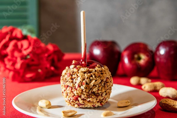 Fototapeta peanut covered red candy apple on white plate with peanuts and apples in background