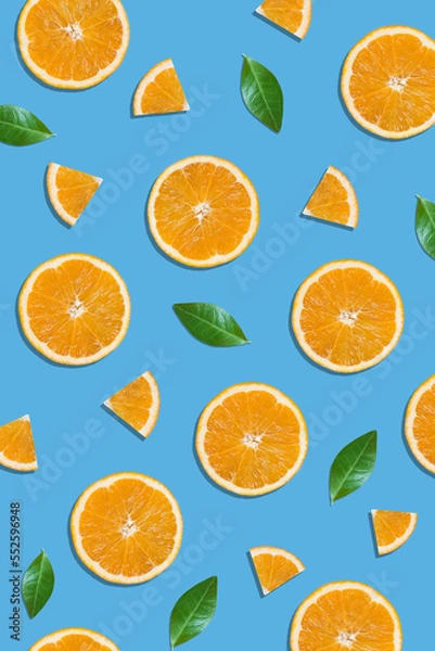 Fototapeta Summer flat lay pattern made with fresh orange fruit slices and green leaves on vibrant blue background. Minimal sunlight concept with sharp shadows.
