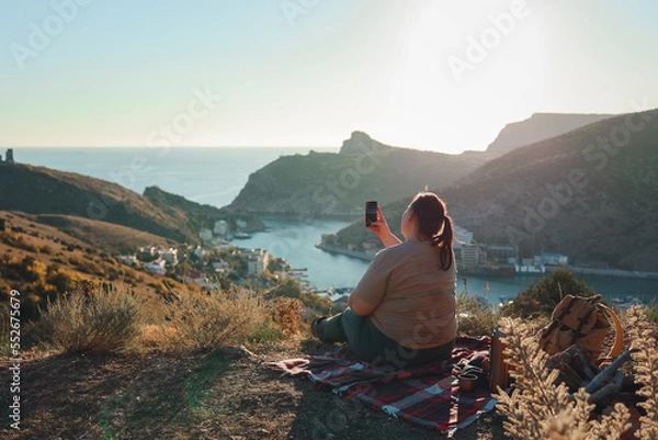 Fototapeta Full girl in an orange jacket, look from the mountain at the sunset.