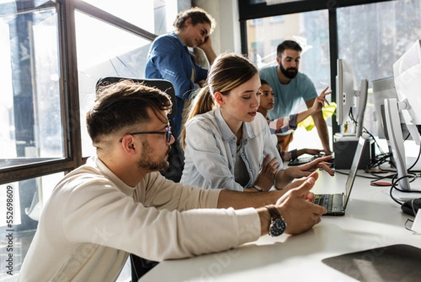 Obraz Group of team workers and game developers  starting a new project. Senior programmer giving help to beginner.	
