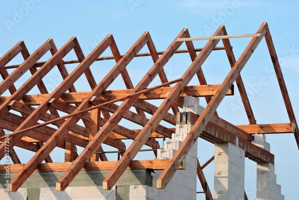 Obraz A timber roof truss, walls made of autoclaved aerated concrete blocks, a reinforced concrete beam and columns, a rough window opening, reinforced brick lintels, blue sky in the background