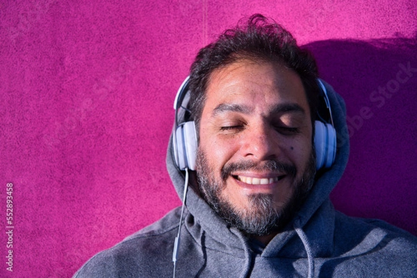 Obraz Portrait of a smiling latin man listening to music in a sunny day.