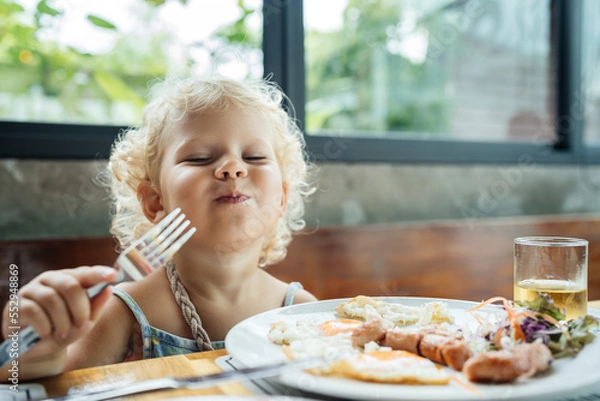 Fototapeta The child is happy to eat food from a plate with an emotion of joy and happiness. Very tasty and fun.
