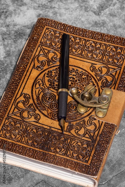 Fototapeta Leather journal, embossed with Celtic tree of life design, with recycled paper and fountain pen. On a dark stone background