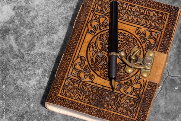 Fototapeta Leather journal, embossed with Celtic tree of life design, with recycled paper and fountain pen. On a dark stone background