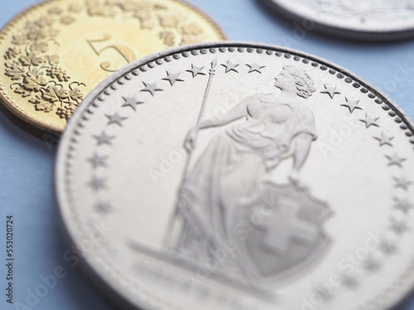 Fototapeta Swiss coins lie on light blue surface. 1 one frank coin close up. Illustration about economy, business or banking. Money and currency of Switzerland. Obverse of coin with figure of Helvetia. Macro