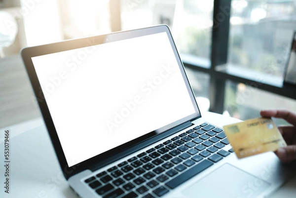 Fototapeta Mockup image of a businesswoman using laptop and holding credit card with blank white desktop screen with coffee cup on wooden table in cafe.