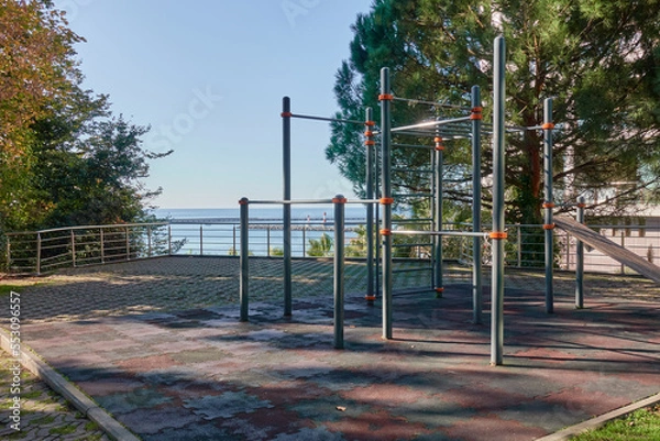 Fototapeta Sports ground on the background of the sea. There are pull-up and push-up machines outside the hotel. Pine and palm trees nearby.