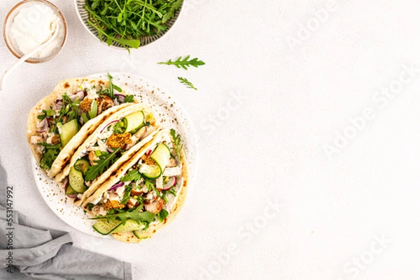 Fototapeta Fried chicken, arugula, cucumber, radish, red onion and wheat tortilla sauce for lunch, delicious Mexican burritos or tacos. Copy space.