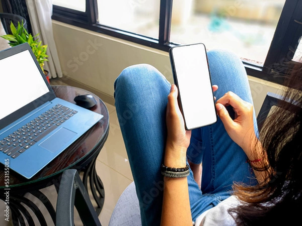 Fototapeta computer, blank screen phone mockup image with white background for advertising, woman's hand using laptop and mobile phone on table in cafe.mockup