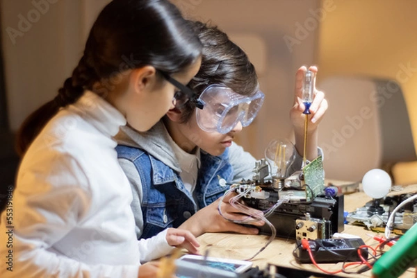 Fototapeta Concentrated boy in protective glasses using screwdriver to fix elements in new electronic device. Girl helping him, giving advice. Electronics, hobby concept