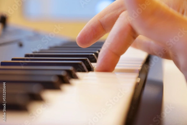 Fototapeta Keyboard keys close up. Right hand finger playing a note in focus. Professional equipment for studio production and live performances. Music production and performance concept.