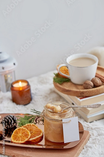 Obraz Homemade salted caramel in glass jar with mockup label among Christmas arrangements and cup of cocoa