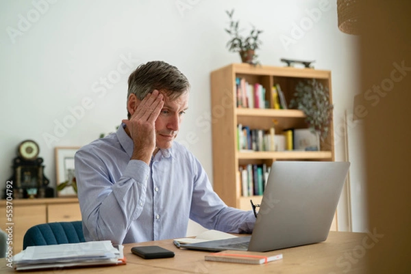 Obraz Senior businessman having a headache while using laptop at home