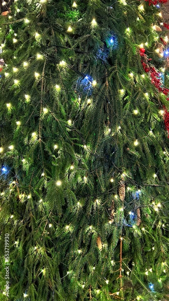 Fototapeta Closeup branches of coniferous tree decorated with glittering balls and shiny garland. Selective focus. Perfect festive content for stories background, vertical banner.