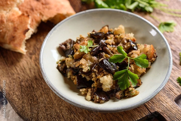 Fototapeta Fried chopped eggplant with garlic and bread crumbs in a bowl on wooden table. Vegetable gourmet snack or appetizer. Selective focus