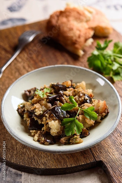 Fototapeta Fried chopped eggplant with garlic and bread crumbs in a bowl on wooden table. Vegetable gourmet snack or appetizer. Selective focus