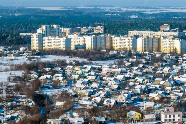 Fototapeta panoramic aerial view of a winter city with a private sector and high-rise residential areas with snow