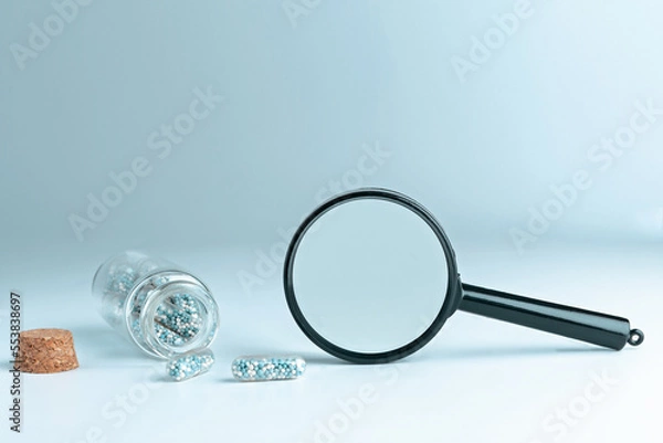Obraz Medical pills and a magnifying glass on a blue background with a copyspace