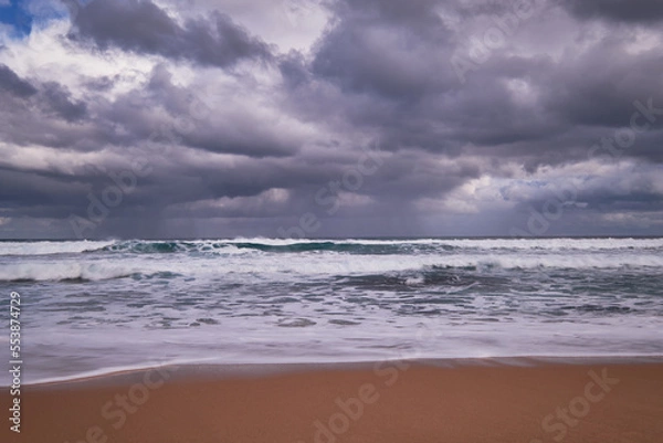 Fototapeta Storm clouds over rough ocean seas with waves breaking onto a sandy beach, beautiful coastal location in Victoria, Australia.
