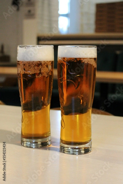 Fototapeta two glasses of foamy light beer in a bar, barley filtered and unfiltered beer, sports bar, beer for a football match, glasses of cool refreshing malt beer in the background of a pub, non-alcoholic