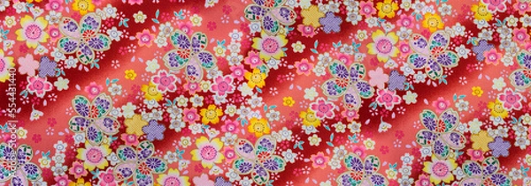 Fototapeta Banner depicting a detailed photograph of a Japanese pattern design illustrated with colorful flowers enhanced with golden color printed on a furoshiki cloth made in cotton fabric on a red background.