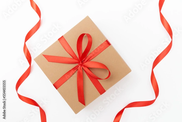 Fototapeta Flat lay of craft present box with red bow and ribbons on the white background