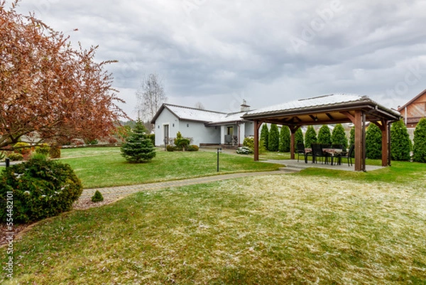 Fototapeta Guest house with green lawn and plants, with a small amount of snow falling
