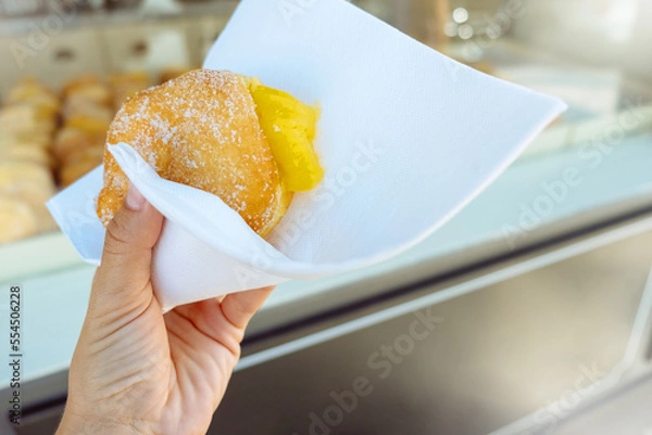 Fototapeta Hand holding Bola de Berlim or Berlim Ball, a Portuguese pastry made from a fried donut filled with sweet eggy cream and rolled in crunchy sugar.