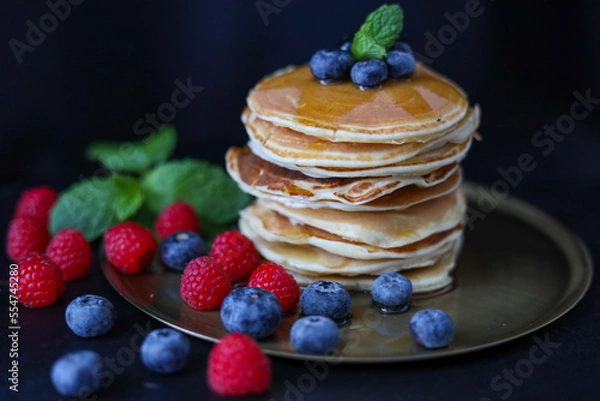 Obraz Pancakes z malinami, miętą i borówkami. Umieszczone są na złotym talerzu i czarnym tle.