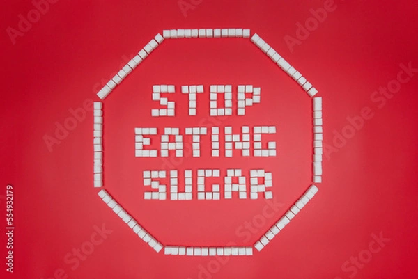 Fototapeta stop eating sugat text in octagonal stop sign shape frame made from sugar cubes. giving up sugar flat lay concept image isolated on red background