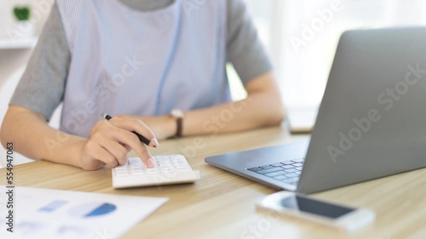 Fototapeta Businesswoman presses a calculator to calculate earnings and analyze company earnings in his private office, Information in finance and accounting, Company performance and revenue.