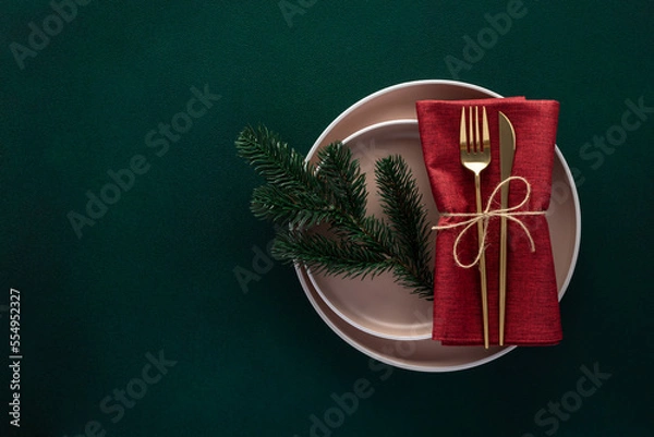 Obraz Christmas or New Year dinner table setting with empty plate and golden cutlery on dark green background, card or menu template with fir tree. Copy space, flat lay design. Top view. Winter holidays.
