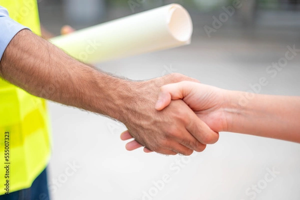 Fototapeta Two engineers shaking hands with deals and success agreements at the construction site. Architect and worker handshaking on construction site.