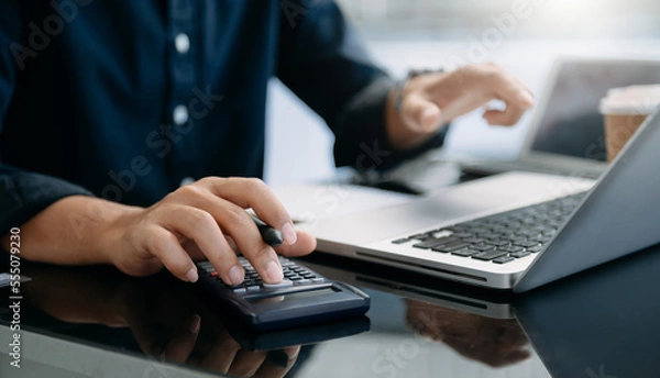 Fototapeta Close up of businesswoman or accountant hand typing laptop working to calculate on desk about cost at home office...