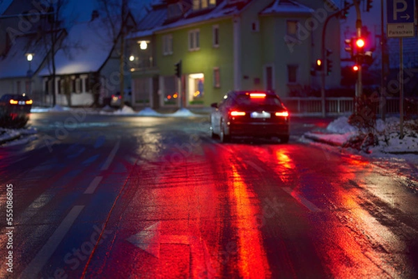 Fototapeta Icy road with ice and snow (Blitzeis, Glatteis). Danger in the morning at road intersection. Vehicle at red light in depth blur. Germany, Nurtingen.