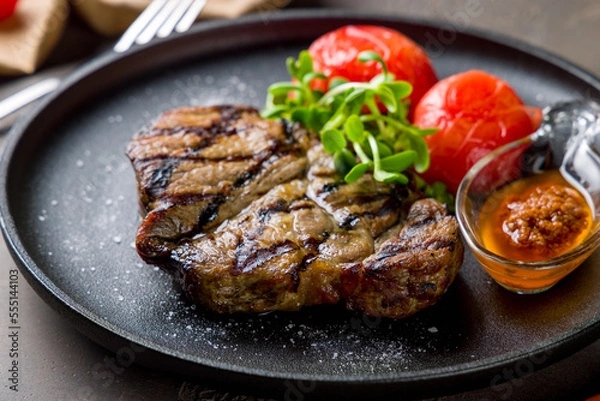 Obraz Fried pork loin with sauce and grilled tomatoes on black plate