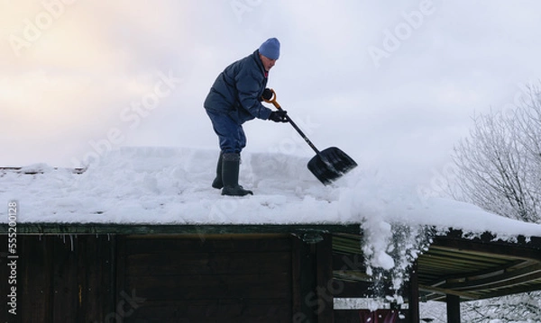 Fototapeta Man in action on the private house roof with shovel cleaning snow. Danger job.