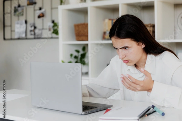 Fototapeta Angry young woman at home office desk work online on computer, have problems with device. Unhappy confused female distressed with laptop troubles, looks desperately, credit card issues while shopping