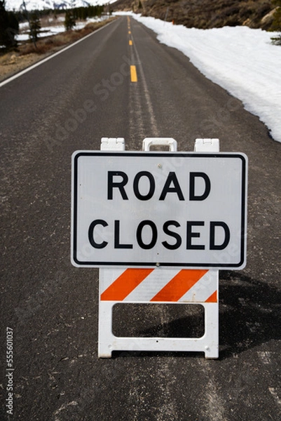 Fototapeta Road closed sign on mountain pass with snow in the background.  Vertical.  