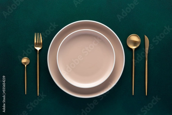 Obraz Festive place setting with beige dishes. Empty plate and gold cutlery on dark green background. Dining table in luxury restaurant. Card or menu template, flat design. Tableware, crockery. Top view.